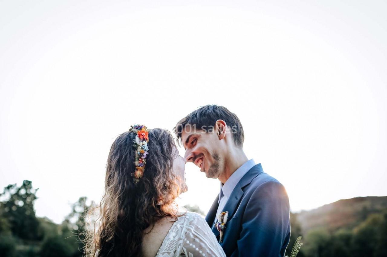Un couple habillé élégamment se regarde avec tendresse en extérieur, sous un ciel clair.