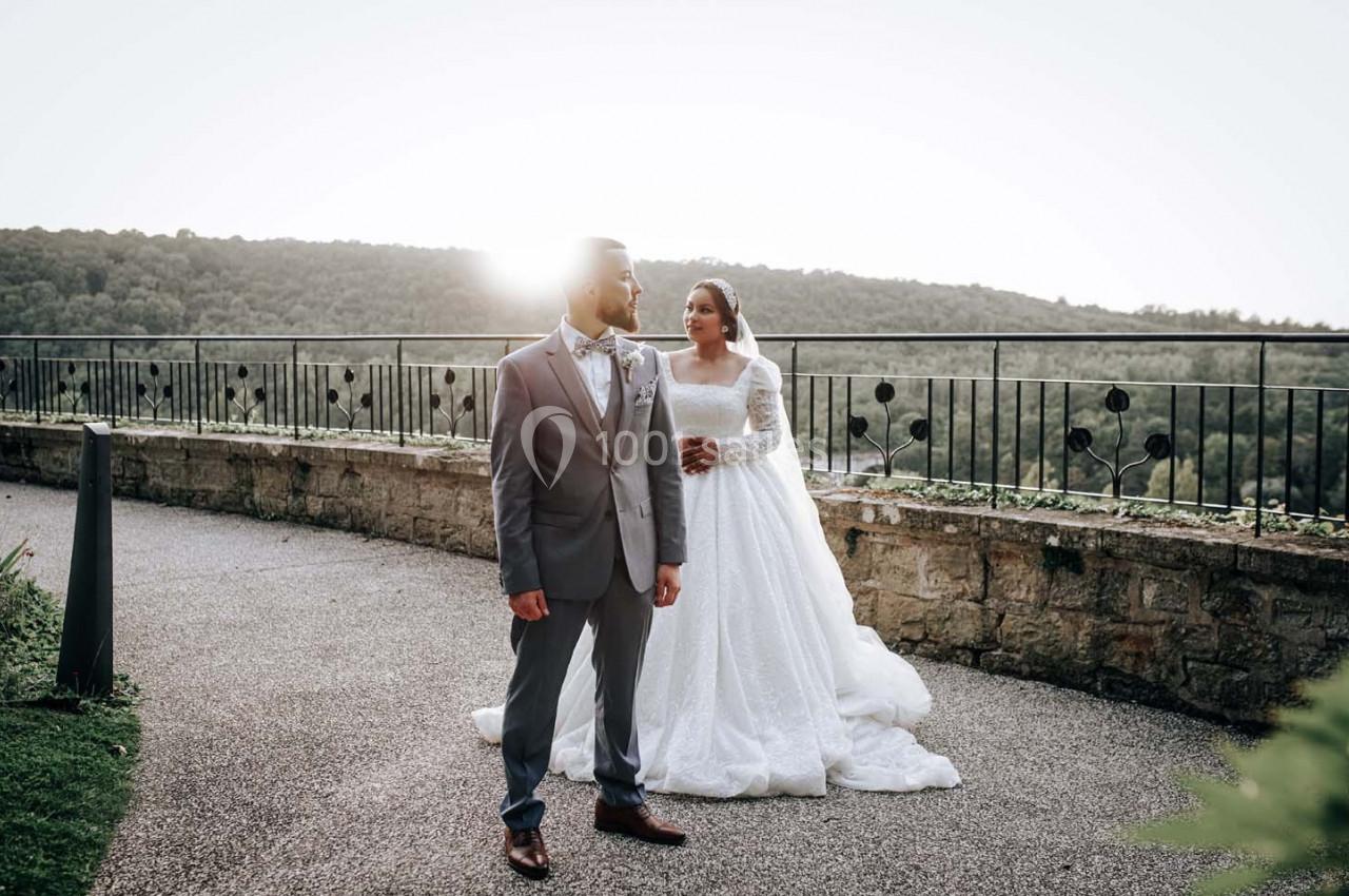 Un couple en tenue de mariage pose devant un paysage naturel avec une lumière du soleil en arrière-plan.