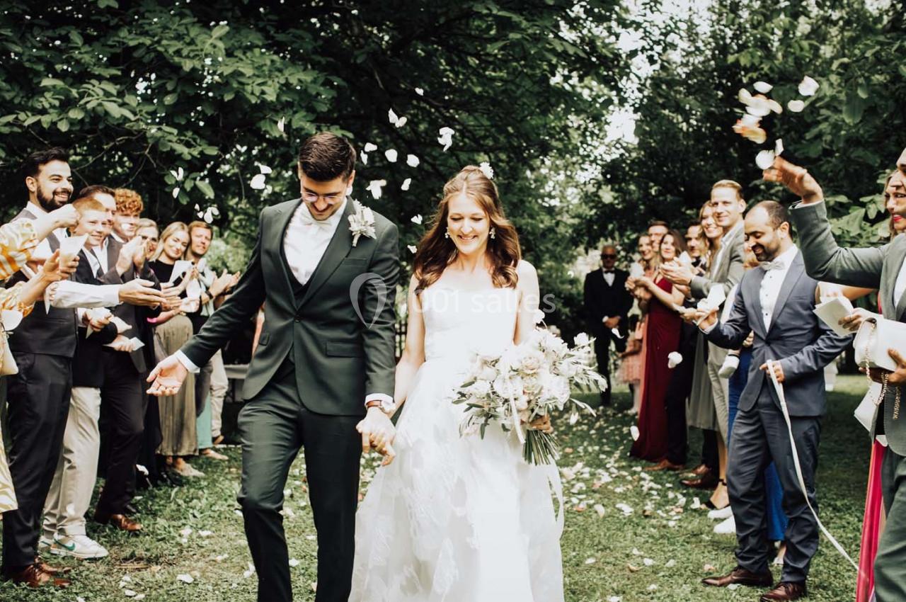 Un couple de mariés souriant marche sous une pluie de pétales, entouré d'invités célébrant dans un jardin verdoyant.