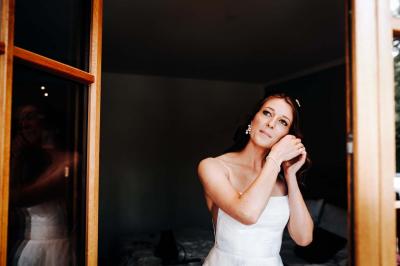 Un couple en tenue de mariage pose devant une voiture ancienne noire et un bâtiment historique entouré de verdure.
