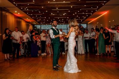 Un couple en tenue de mariage pose devant une voiture ancienne noire et un bâtiment historique entouré de verdure.