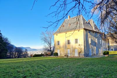 Manoir ancien entouré d'arbres dénudés en hiver, situé dans un parc verdoyant sous un ciel bleu clair.