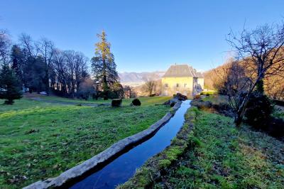 Manoir ancien entouré d'arbres dénudés en hiver, situé dans un parc verdoyant sous un ciel bleu clair.