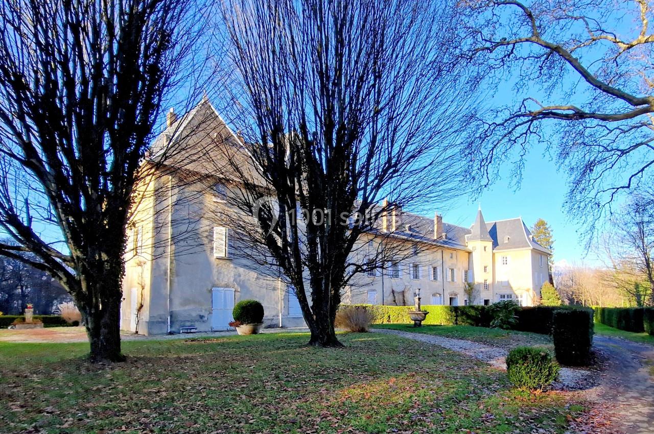 Façade d'un château entouré d'arbres dénudés en hiver, avec pelouse et allée gravillonnée au premier plan.