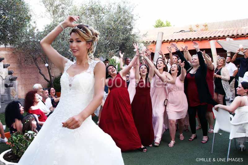 Une mariée souriante avance tandis qu'un groupe de femmes derrière elle tente d'attraper son bouquet lancé.