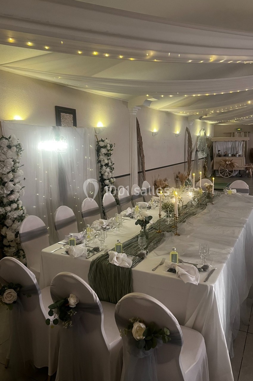 Location salle Cuers (Var) - L'atrium #8 Salle de réception décorée avec une table de banquet ornée de bougies, fleurs blanches et guirlandes lumineuses au plafond.