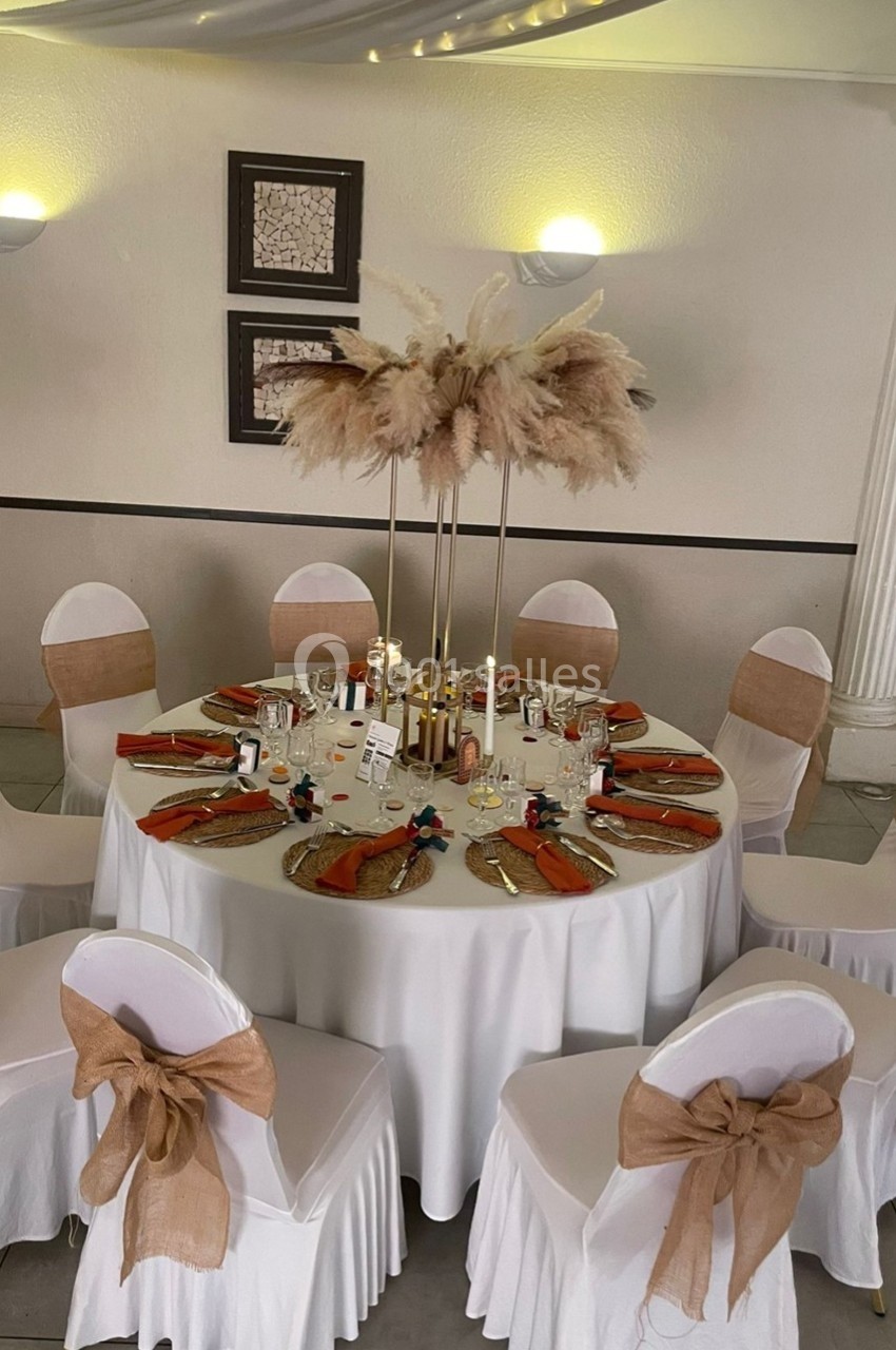 Location salle Cuers (Var) - L'atrium #7 Table ronde décorée pour un événement, avec nappes blanches, chaises ornées de nœuds en toile de jute et centre de table…