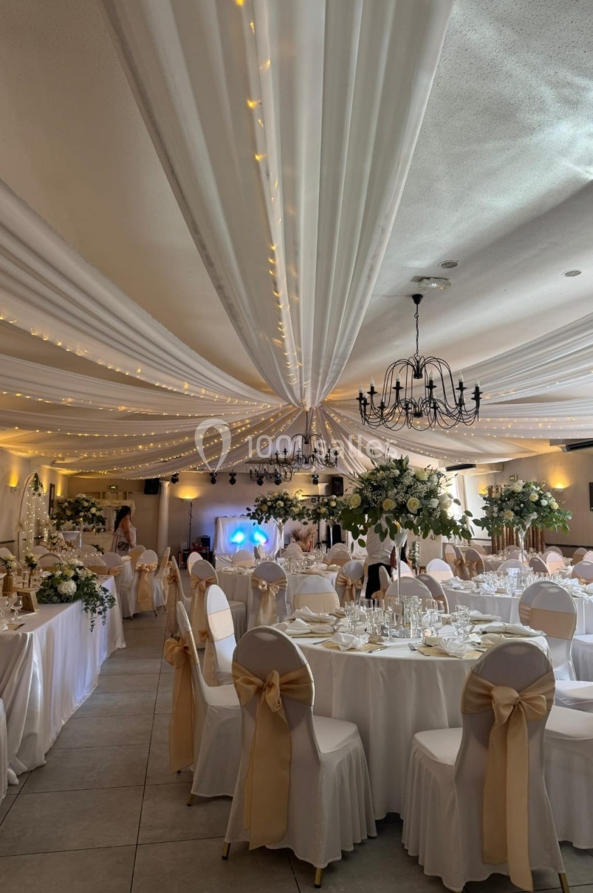 Location salle Cuers (Var) - L'atrium #26 Salle de réception décorée avec des tables rondes, nappes blanches, chaises ornées de rubans dorés et guirlandes lumineuses.
