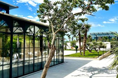 Terrasse extérieure avec tables, chaises, parasol, plantes et vue sur un bâtiment vitré sous un ciel dégagé.