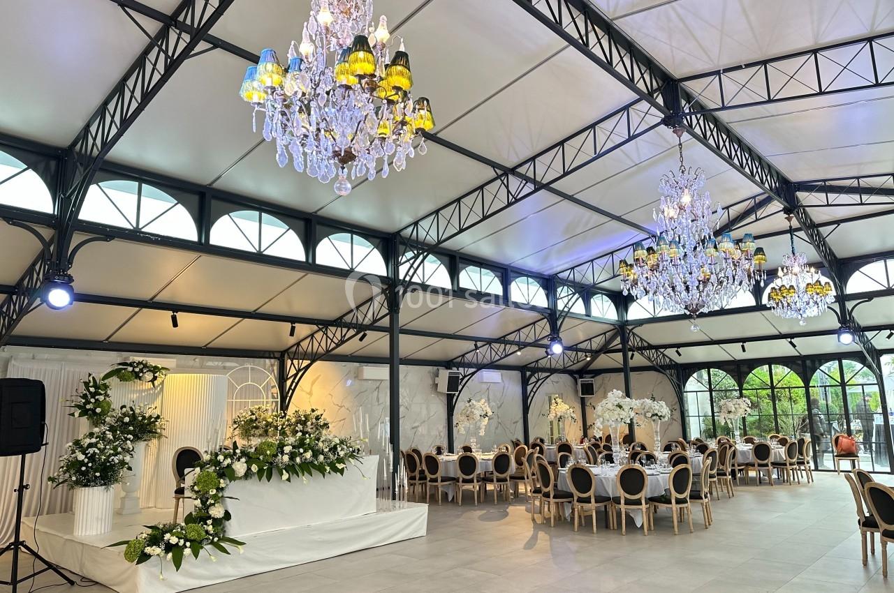 Salle de réception élégante avec tables décorées, lustres imposants et espace fleuri pour une cérémonie ou un événement.