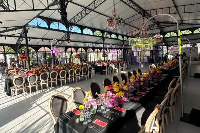 Terrasse extérieure avec tables, chaises, parasol, plantes et vue sur un bâtiment vitré sous un ciel dégagé.