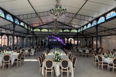 Terrasse extérieure avec tables, chaises, parasol, plantes et vue sur un bâtiment vitré sous un ciel dégagé.