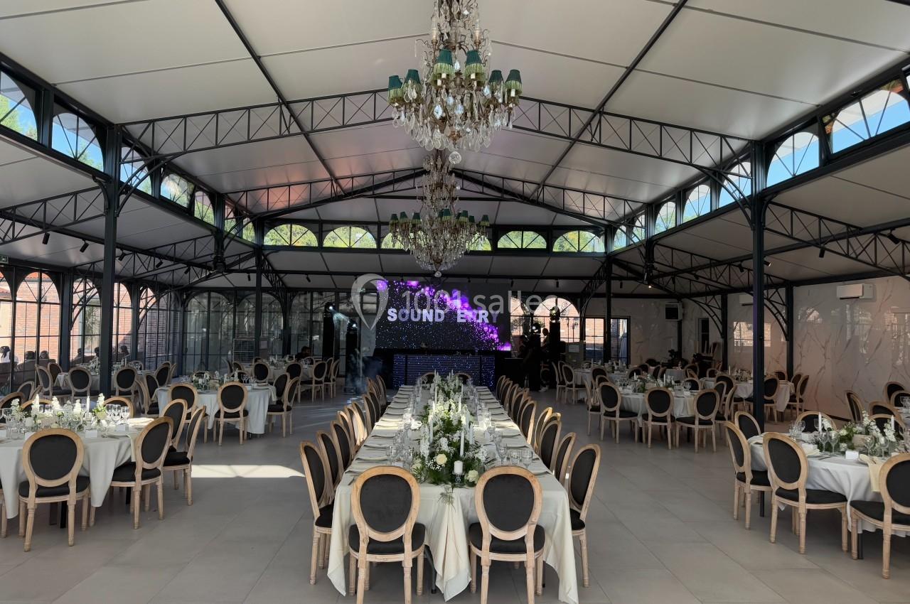 Salle de réception lumineuse avec tables élégamment dressées, chaises en bois et grand écran en fond.