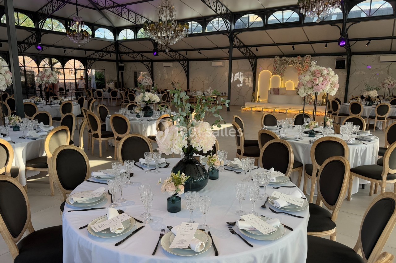 Salle de réception élégante avec tables rondes dressées, décor floral et éclairage chaleureux.