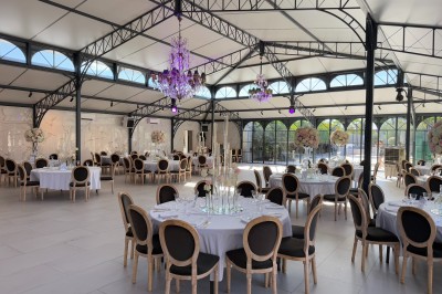 Terrasse extérieure avec tables, chaises, parasol, plantes et vue sur un bâtiment vitré sous un ciel dégagé.