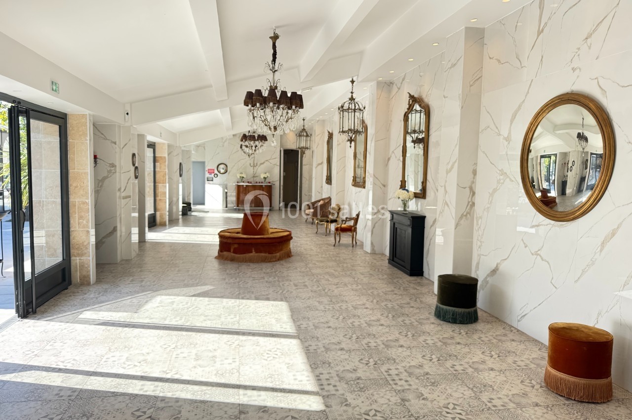 Hall lumineux avec sol en carrelage clair, murs en marbre, miroirs dorés, lustres et mobilier élégant.