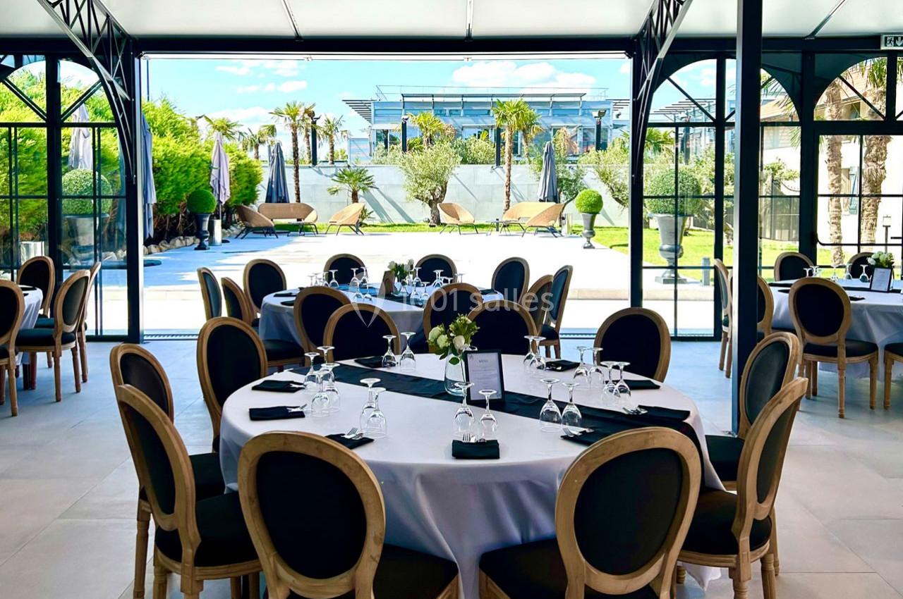 Salle de réception élégante avec tables dressées, donnant sur une terrasse avec piscine et jardin arboré.