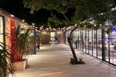Miniature Location salle Bobigny (Seine-Saint-Denis) - Orangerie du Manoir des Vignes #10 Allée extérieure éclairée la nuit, bordée de plantes, d'un arbre et de bâtiments vitrés illuminés.