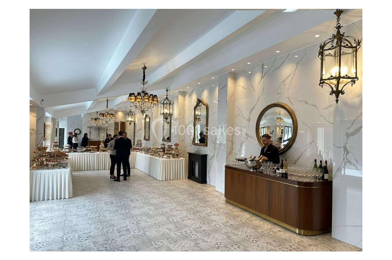 Location salle Bobigny (Seine-Saint-Denis) - Orangerie du Manoir des Vignes #4 Salle élégante avec tables de buffet garnies, lustres suspendus, miroirs ronds et un serveur près d'un bar.