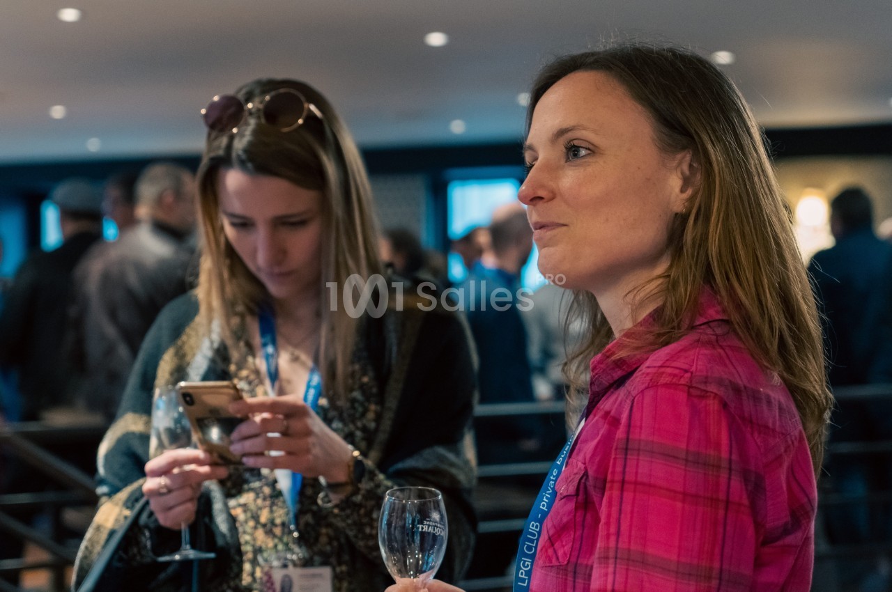 Deux femmes discutent lors d'un événement, l'une tenant un verre et l'autre regardant son téléphone.
