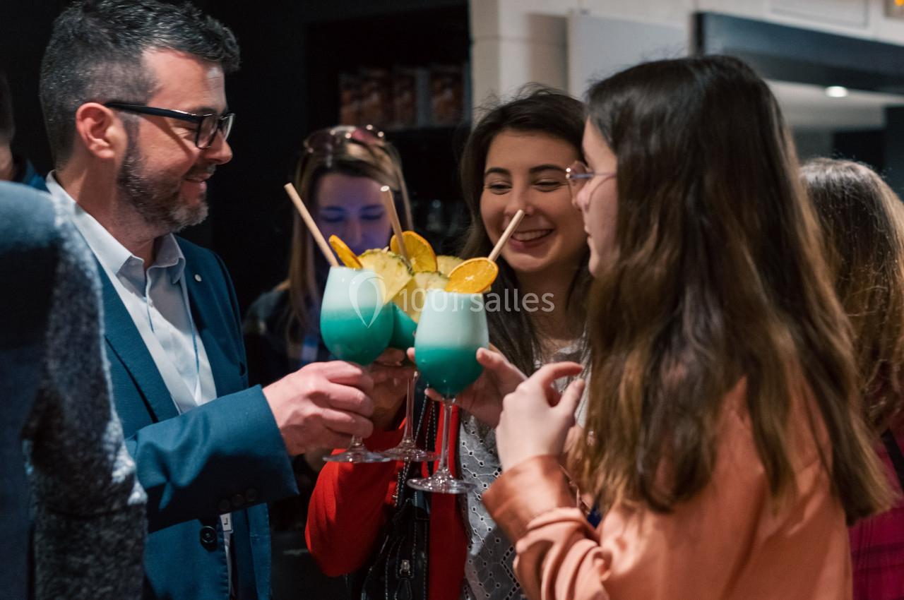 Un groupe de personnes trinque avec des cocktails colorés dans un cadre intérieur convivial.