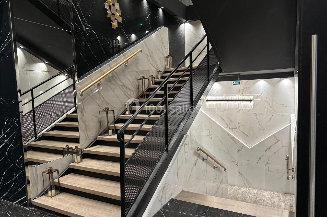 Escalier intérieur moderne en marbre clair avec rampes noires et éclairage intégré dans un espace élégant.