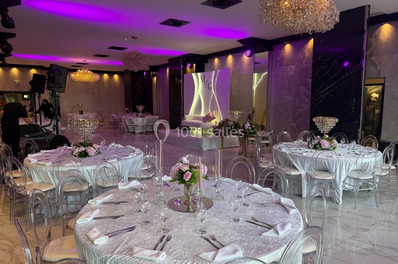 Salle de réception élégante avec tables rondes dressées, éclairage violet et décoration florale raffinée.
