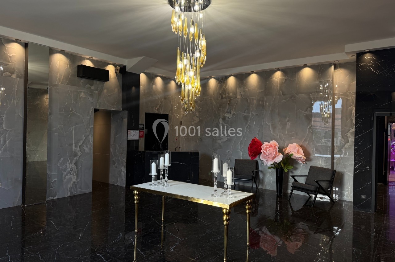 Hall moderne avec sol en marbre noir, table décorée de bougies et fleurs, éclairée par un lustre doré.