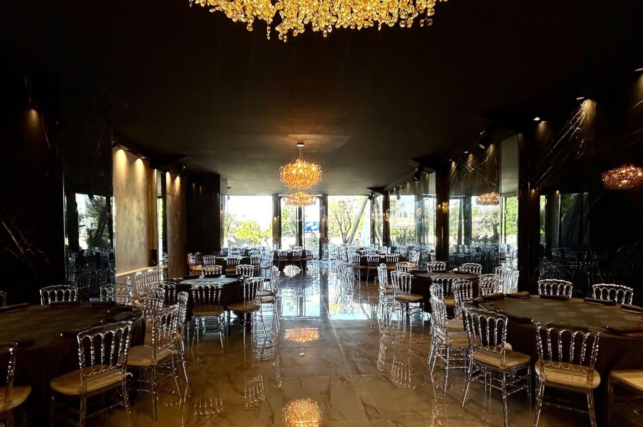 Salle de réception élégante avec des lustres en cristal, des tables rondes et des chaises transparentes sur un sol brillant.