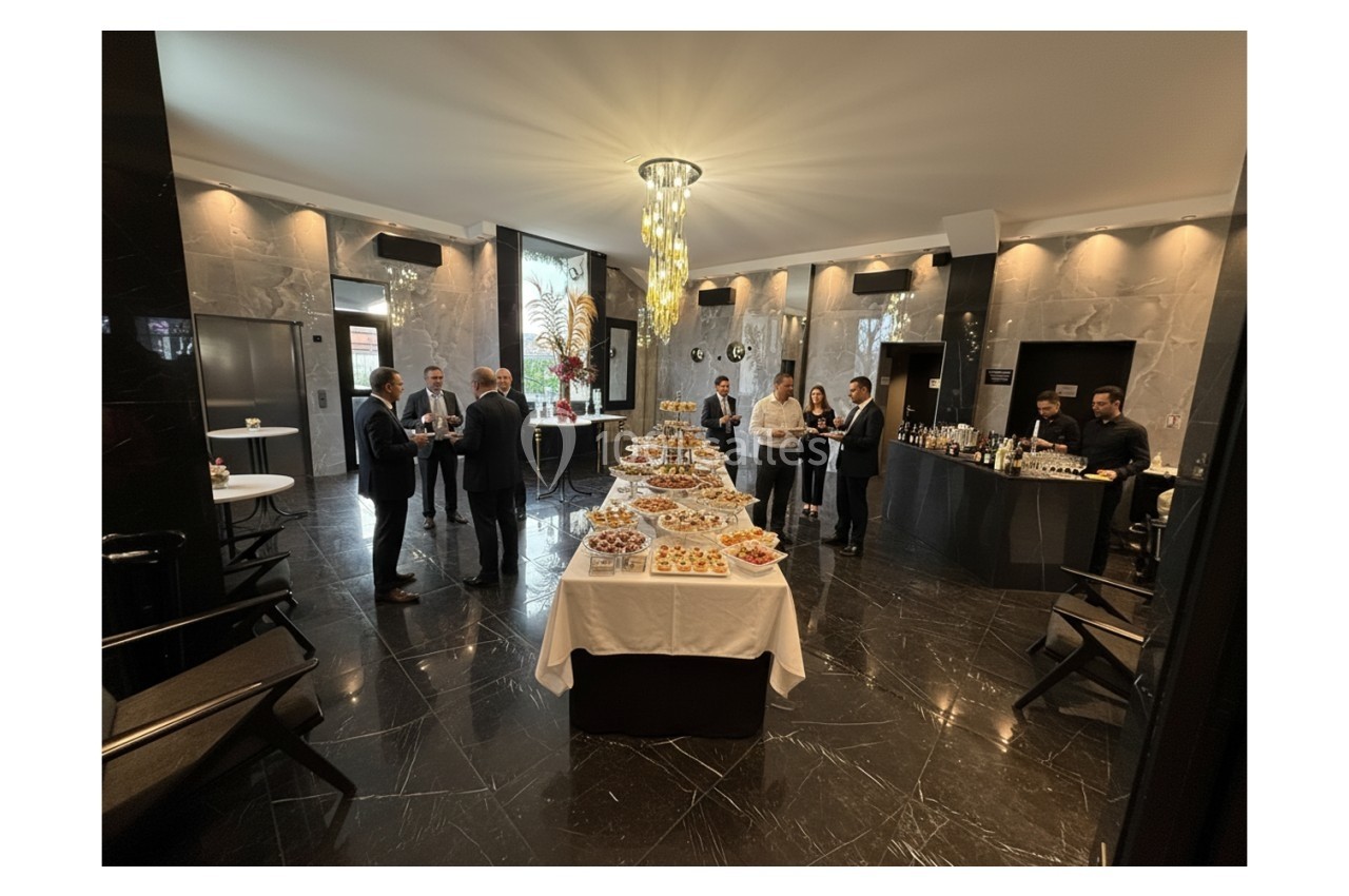 Salle élégante avec buffet de desserts au centre, quelques personnes discutant debout autour.