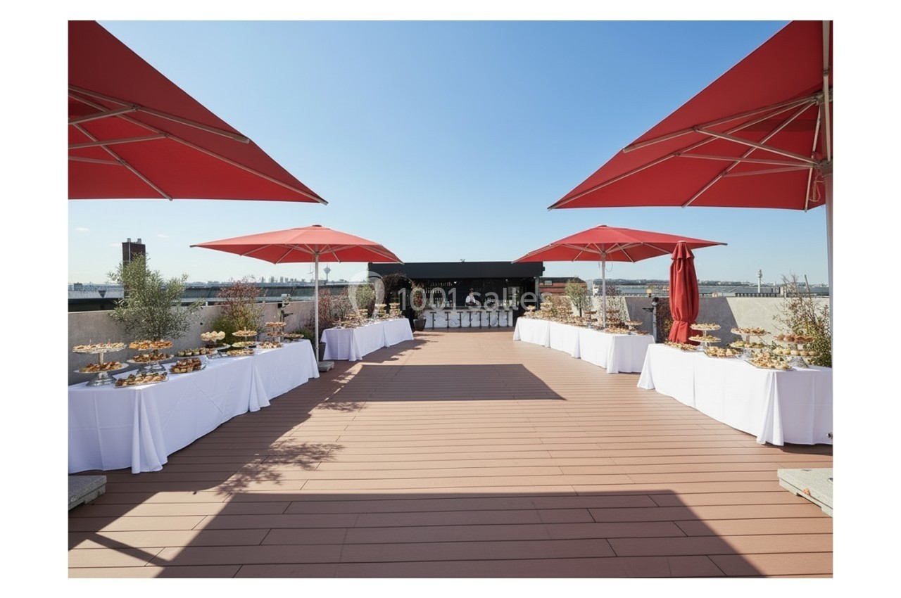 Terrasse ensoleillée aménagée pour un événement, avec tables dressées et parasols rouges.