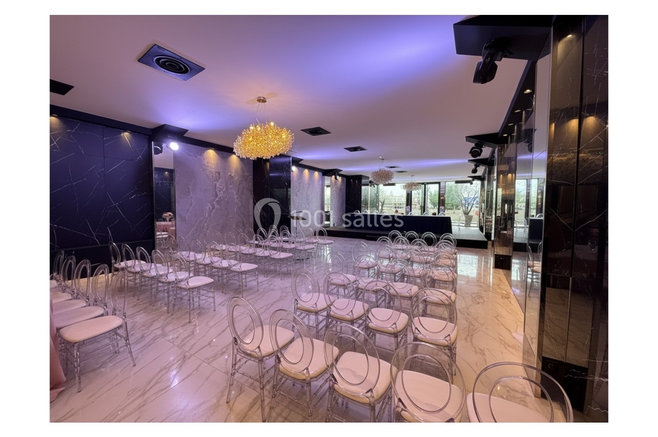 Salle de réception moderne avec chaises transparentes, sol en marbre, murs sombres et éclairage tamisé.