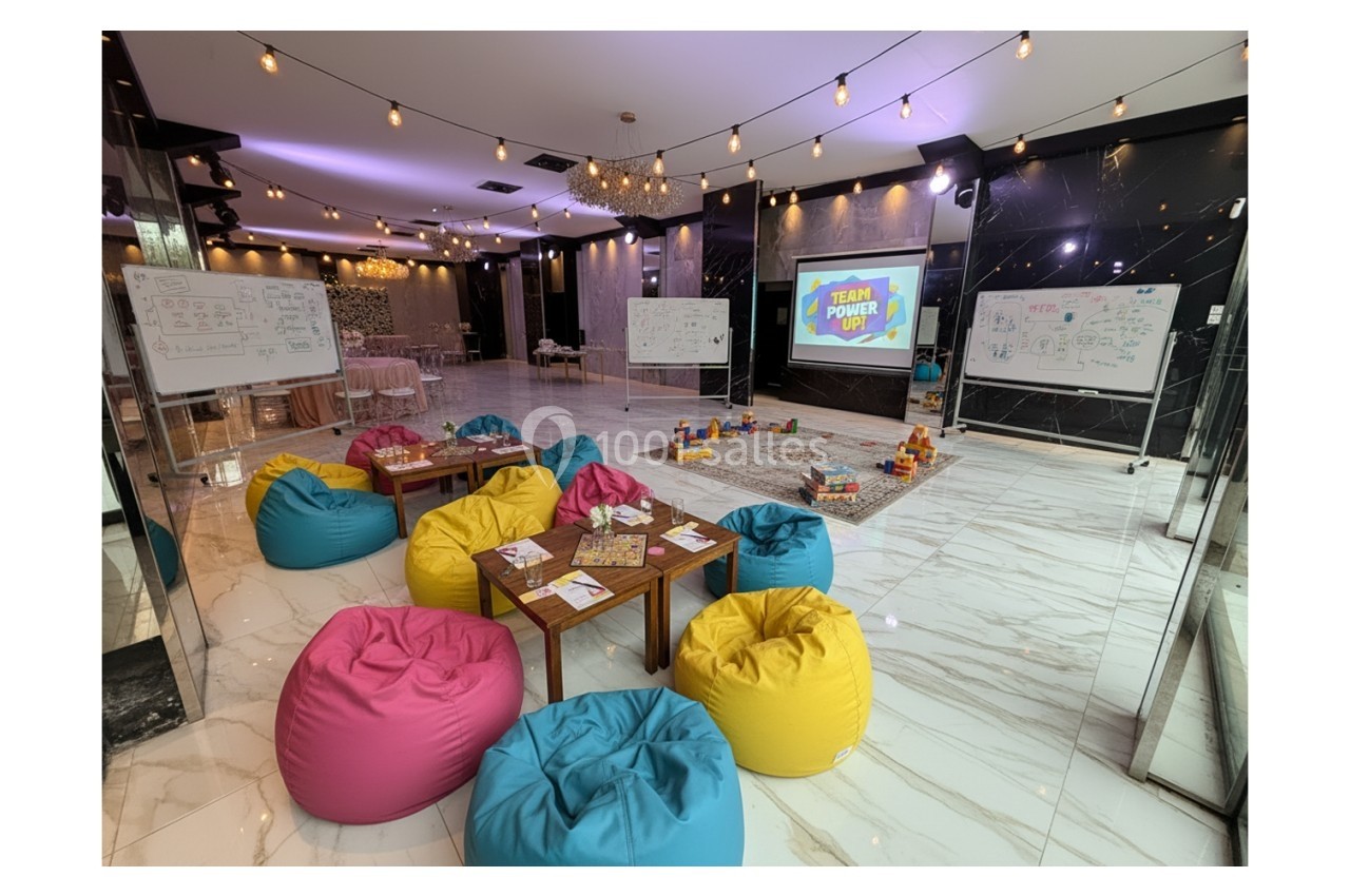 Salle aménagée avec poufs colorés, tables basses, tableaux blancs et écran affichant ’Team Power’, ambiance conviviale.