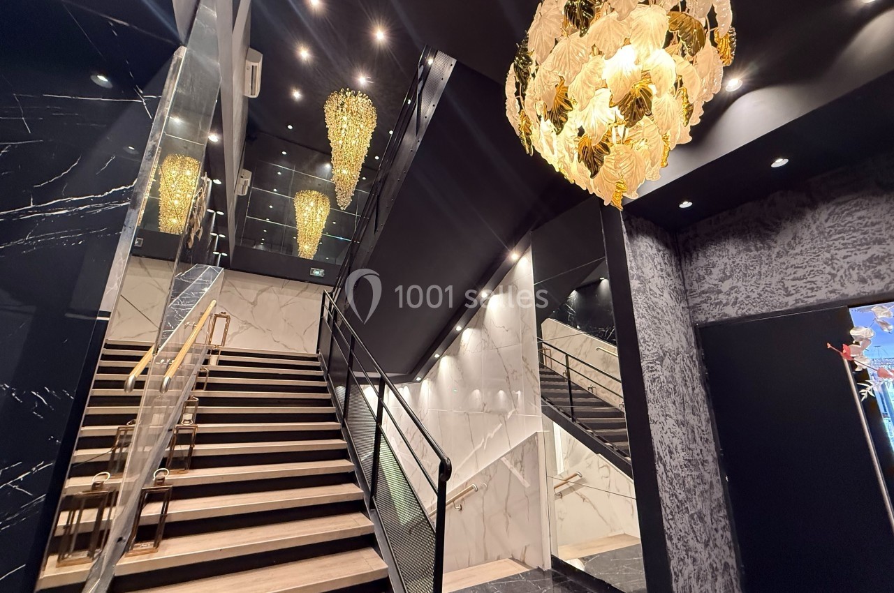 Escalier intérieur élégant avec murs en marbre, miroirs, et lustres dorés suspendus dans un espace moderne.