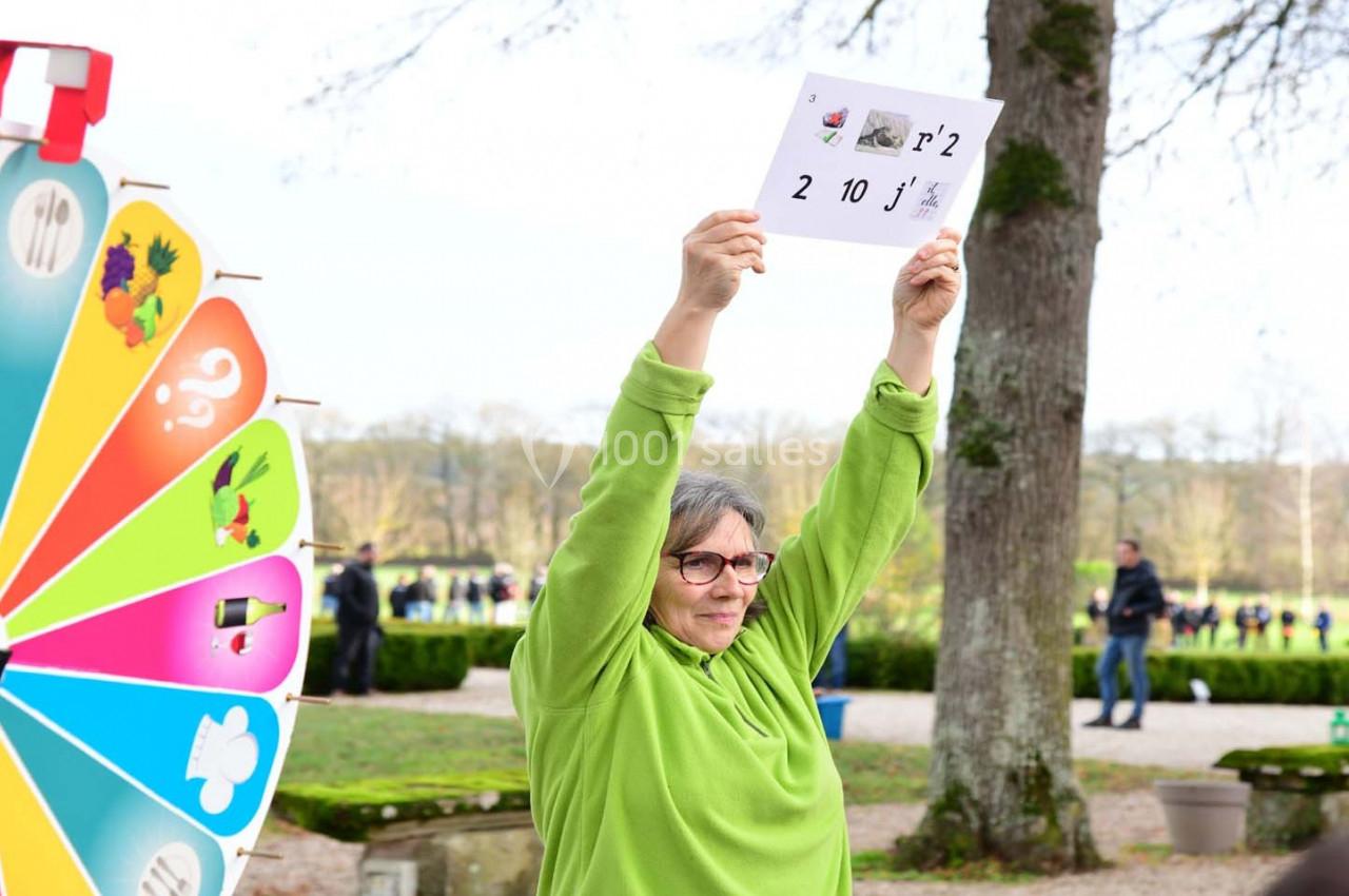Une personne en vert tient une feuille avec des chiffres et des symboles, près d'une roue colorée, dans un parc.