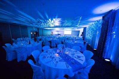 Salle de conférence avec rangées de chaises colorées, un pupitre à l'avant et des panneaux en bois en arrière-plan.