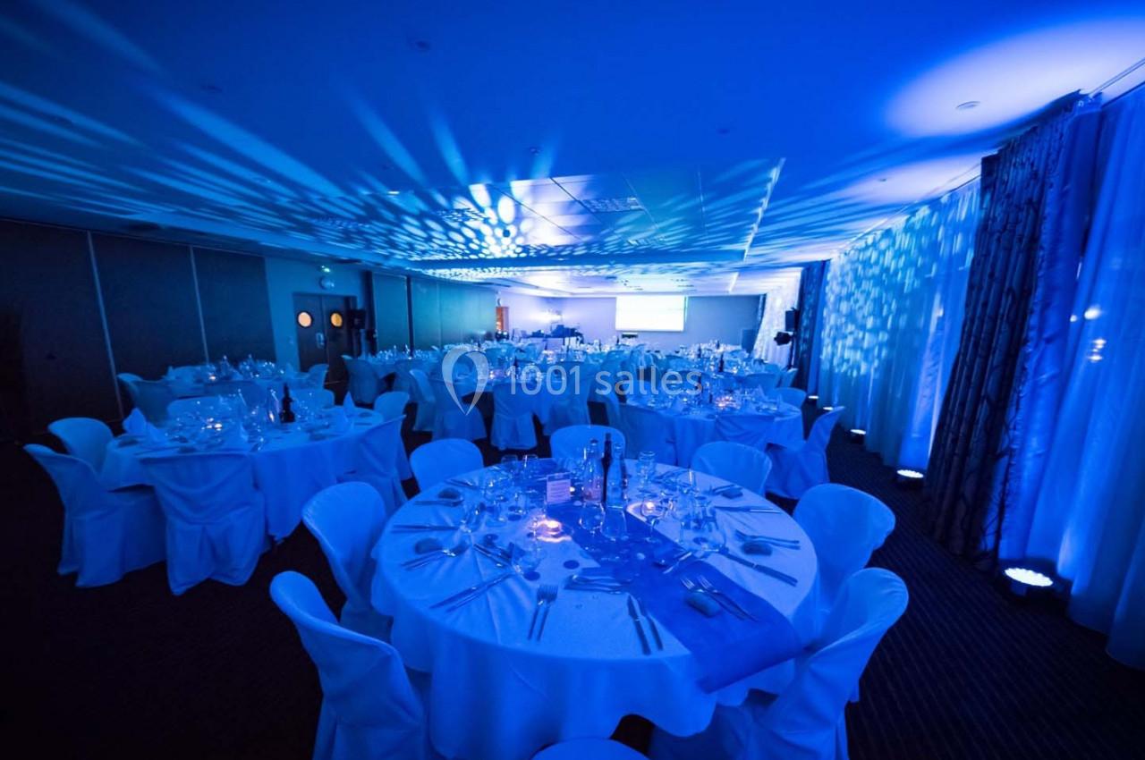 Salle de réception éclairée en bleu avec tables rondes dressées pour un événement formel.