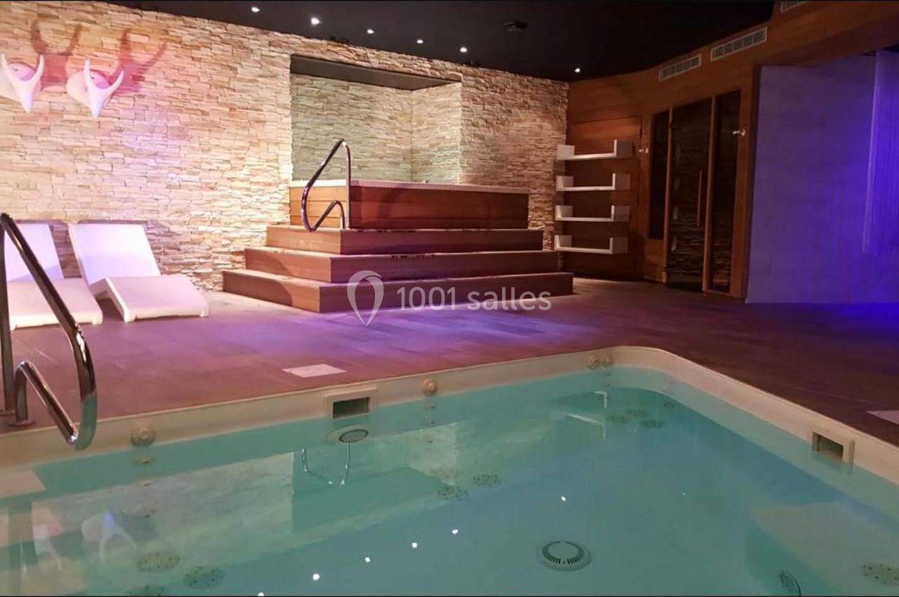 Piscine intérieure avec bain à remous, chaises longues blanches et murs en pierre dans un espace spa moderne.