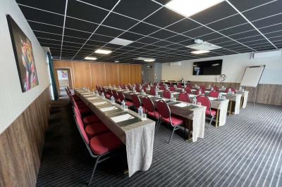 Salle de conférence avec rangées de chaises colorées, un pupitre à l'avant et des panneaux en bois en arrière-plan.