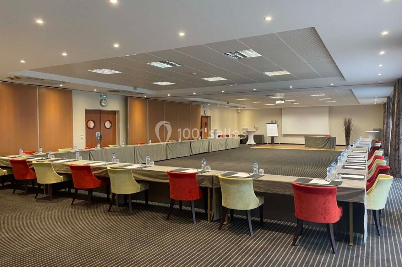 Salle de réunion spacieuse avec tables disposées en U, chaises colorées et équipement de présentation.