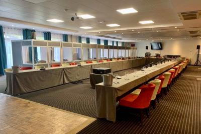 Salle de conférence avec rangées de chaises colorées, un pupitre à l'avant et des panneaux en bois en arrière-plan.