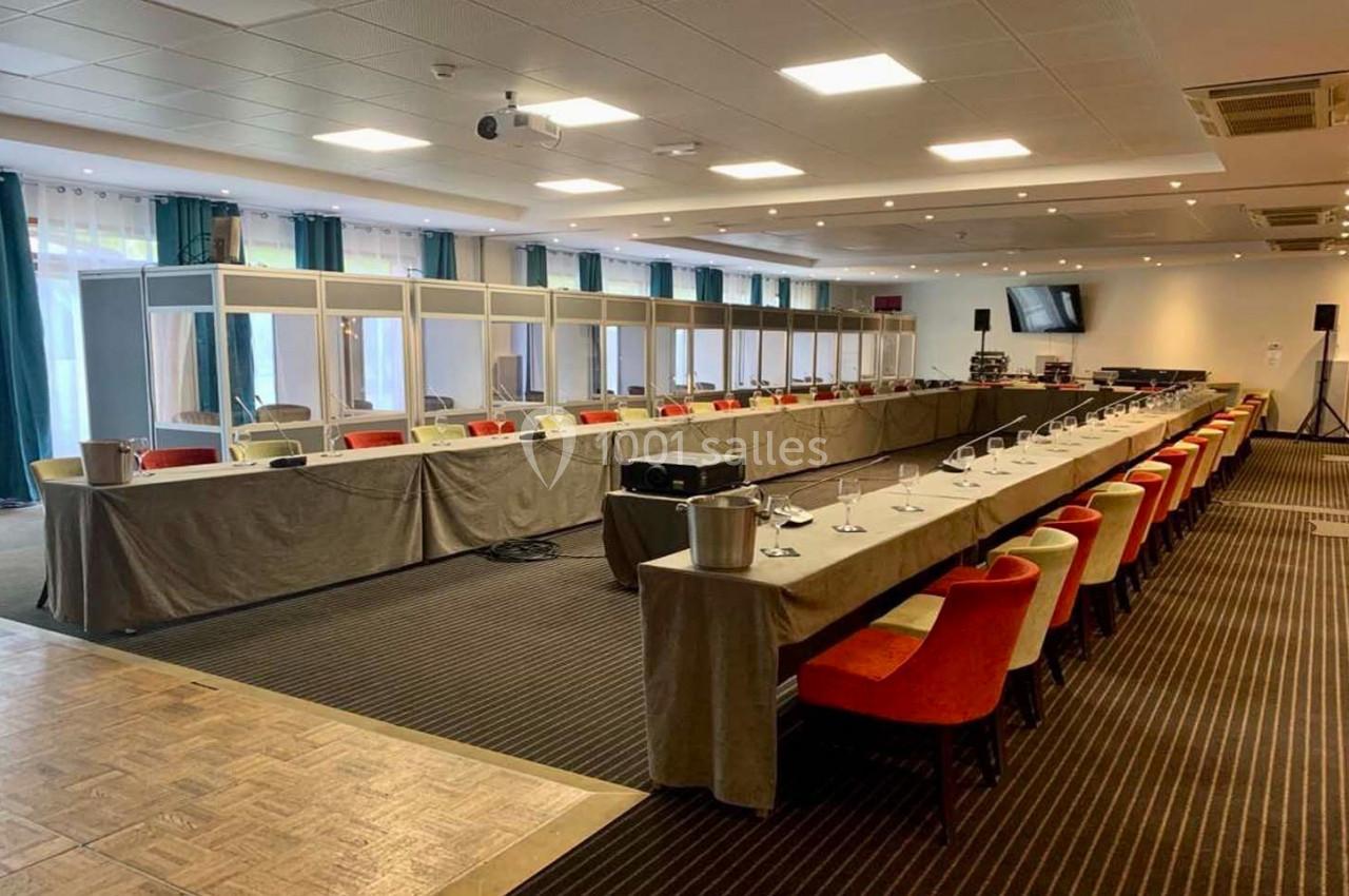 Salle de conférence équipée de cabines d'interprétation, tables en U avec micros et chaises colorées.
