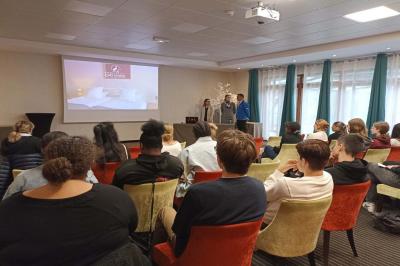Salle de conférence avec rangées de chaises colorées, un pupitre à l'avant et des panneaux en bois en arrière-plan.