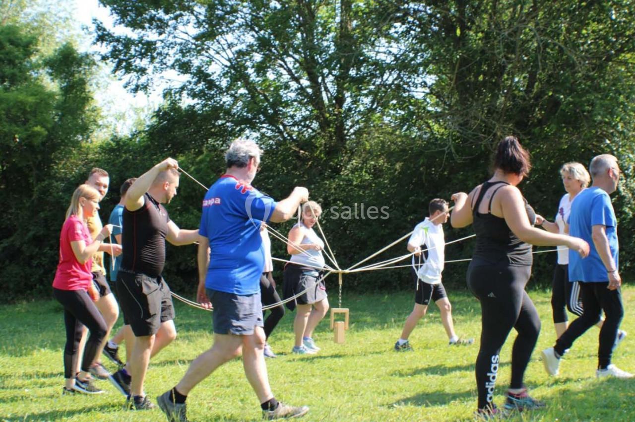 Un groupe de personnes participe à une activité collaborative en extérieur, manipulant des cordes dans un espace herbeux.
