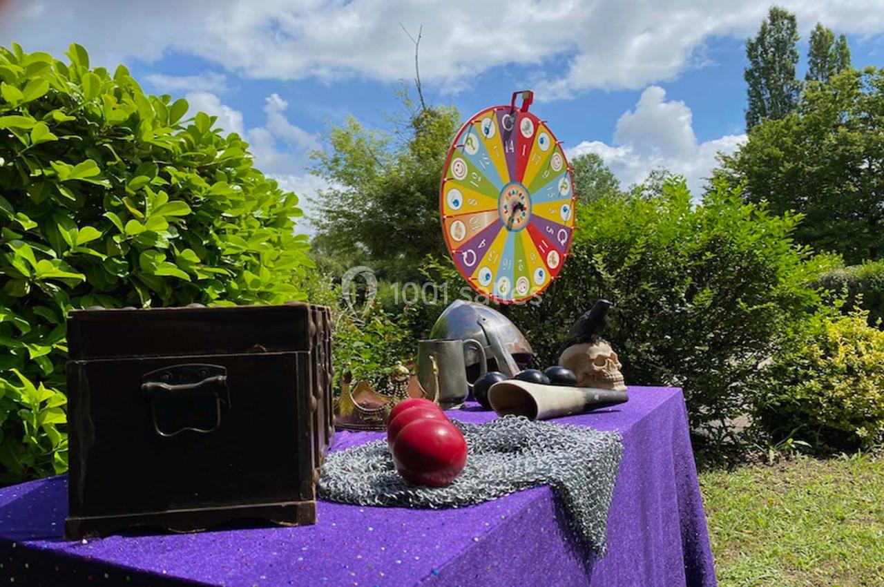 Table avec objets variés, roue colorée en arrière-plan, disposée dans un jardin verdoyant sous un ciel partiellement nuageux.
