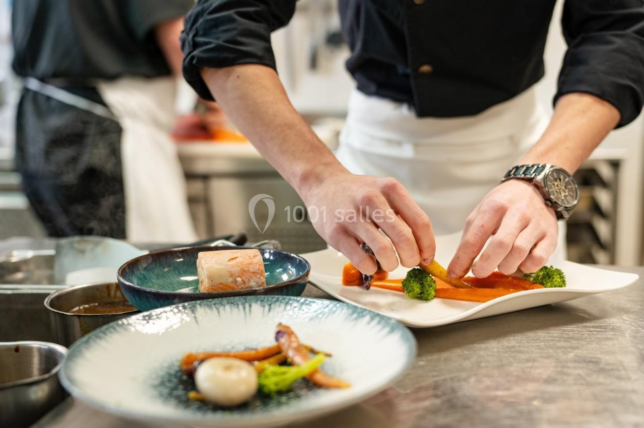 Un chef dispose soigneusement des légumes sur une assiette dans une cuisine professionnelle.