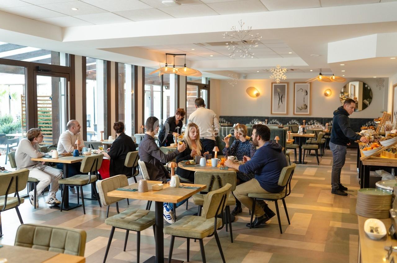 Salle de restaurant lumineuse avec des clients attablés, discutant et prenant leur repas dans une ambiance conviviale.