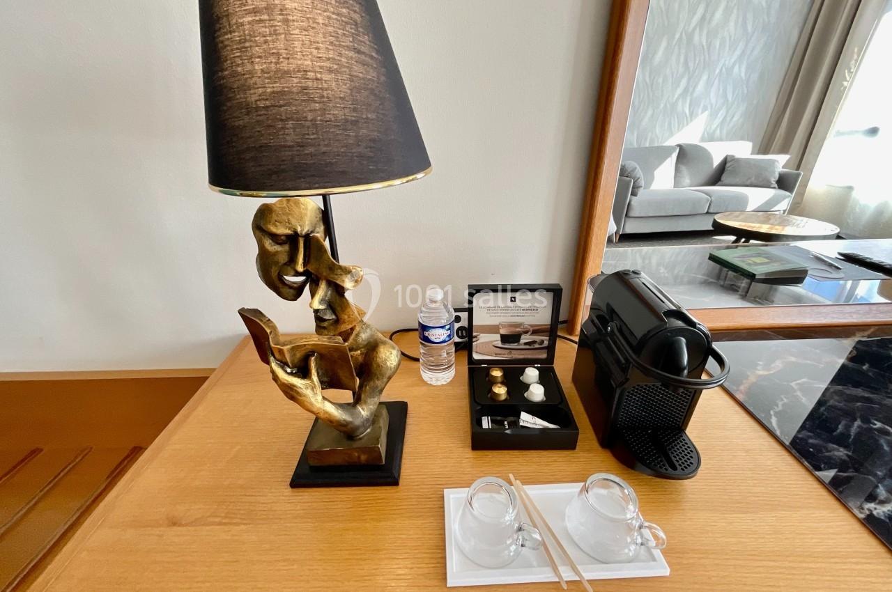 Lampe sculptée en métal doré sur une table en bois avec machine à café, tasses, capsules et bouteille d'eau.