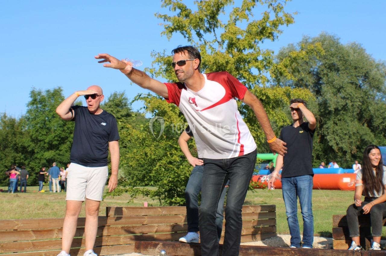 Un homme lance un objet lors d'une activité en plein air, entouré de spectateurs dans un cadre verdoyant.