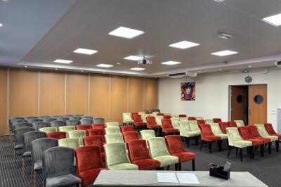 Salle de conférence avec rangées de chaises colorées, un pupitre à l'avant et des panneaux en bois en arrière-plan.